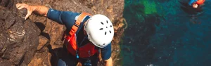 Guía de coasteering ayudando a un visitante durante una sección de escalada costera