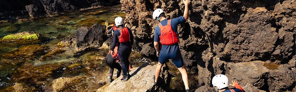 Group of coasteering participants wearing helmets and life jackets exploring rocky coastal formations in Ibiza.